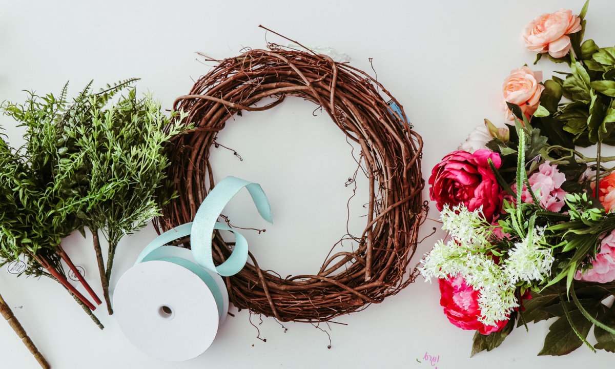 An empty wreath and craft supplies liike ribbon and flowers on a tabletop.