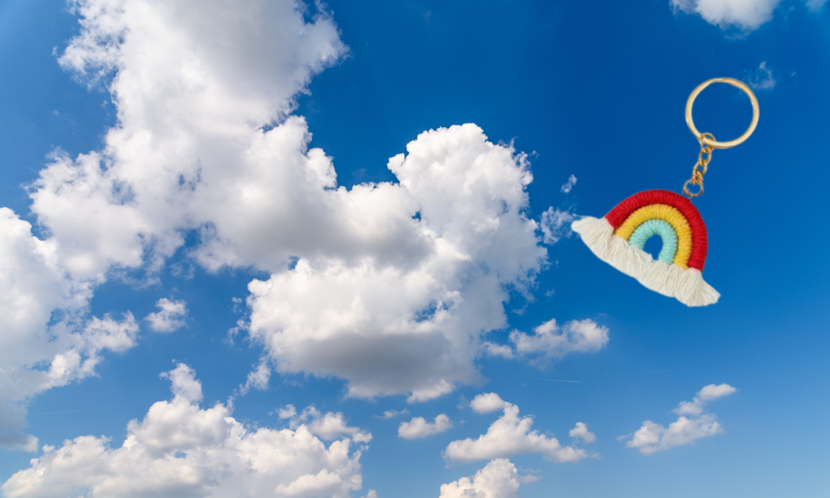 Macrame rainbow keychain on a cloudy, blue sky backdrop.